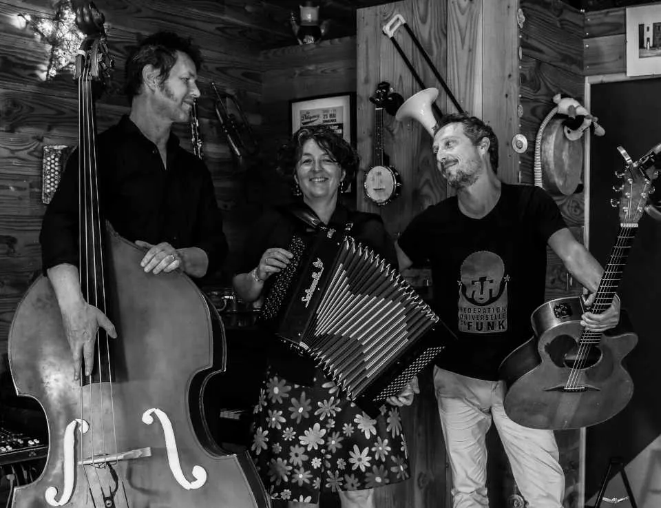 The Jukebal trio in a studio, black and white, Alexandre Roux on double bass, Marilou Emerial on accordion, Julien Régi on guitar
